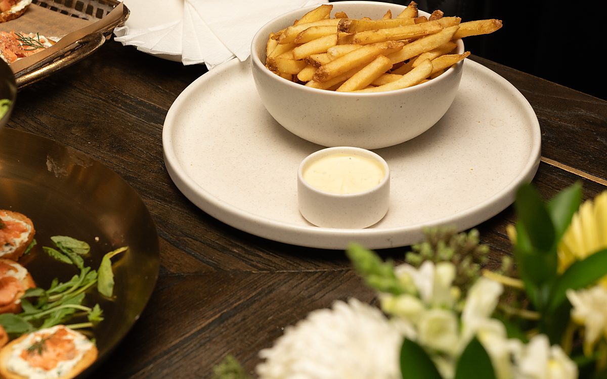 A bowl of fries with aioli on a stone plate, fresh flowers alongside