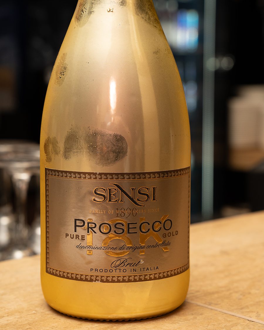 A gold bottle of Prosecco on the bar, glasses waiting behind it