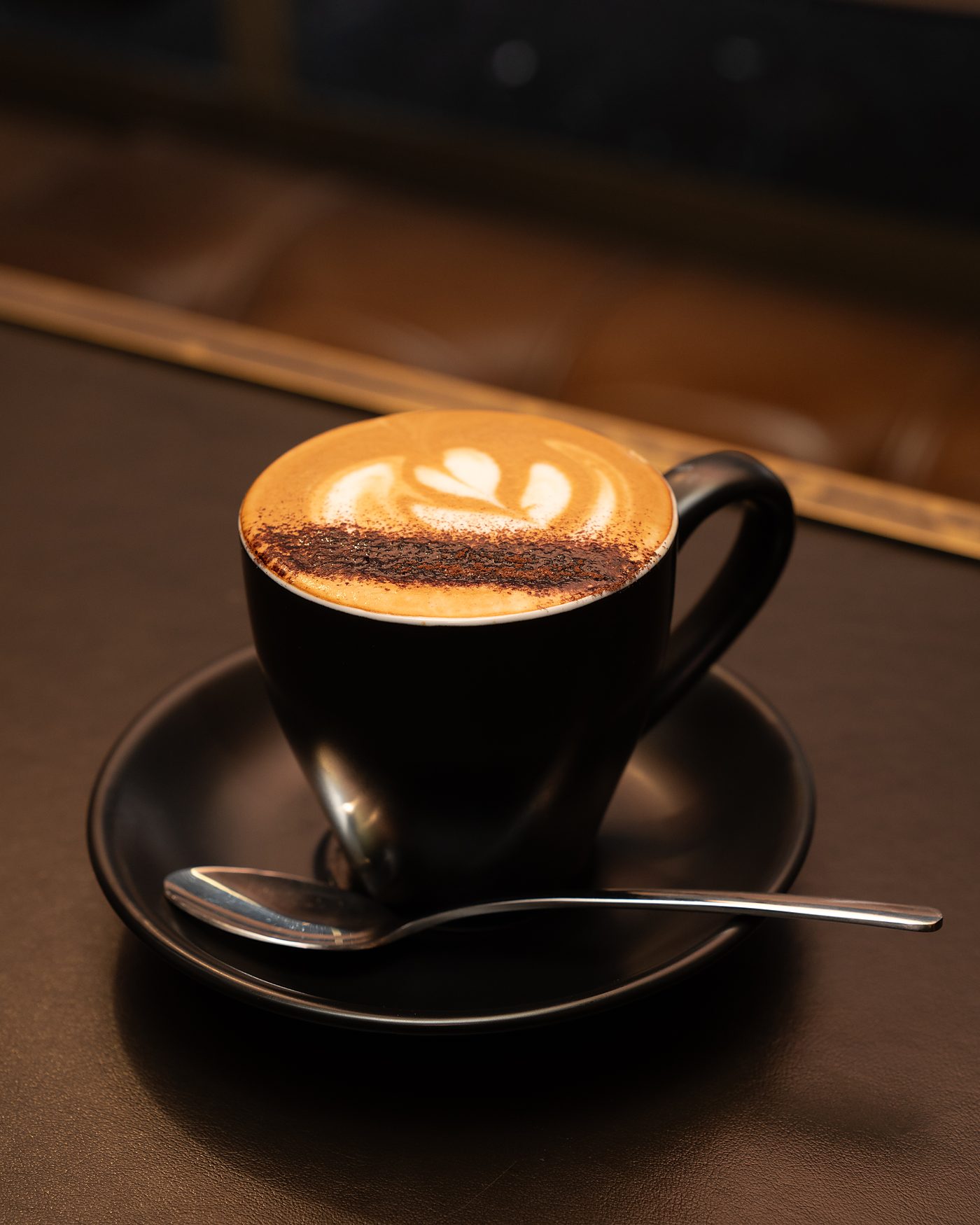 A flat white with latte art in a black cup on the bar at Deschlers