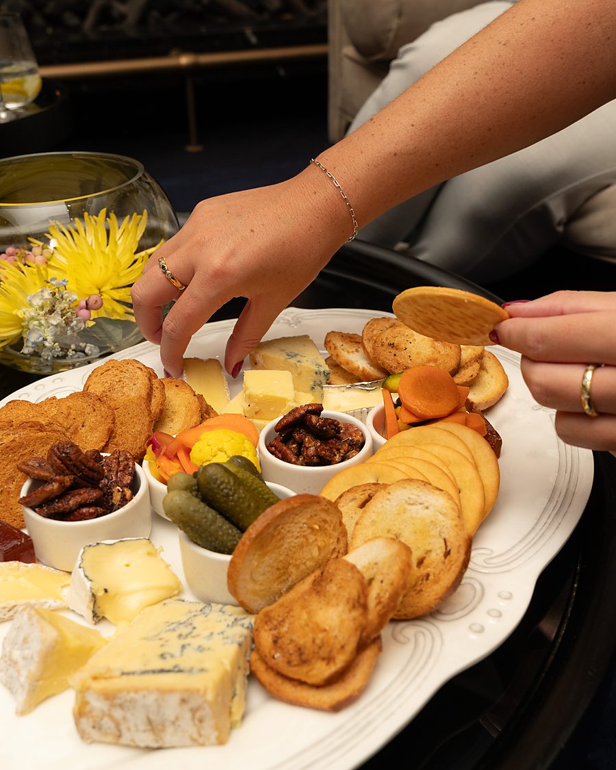 Guests reaching for cheese and crostini on a grazing platter